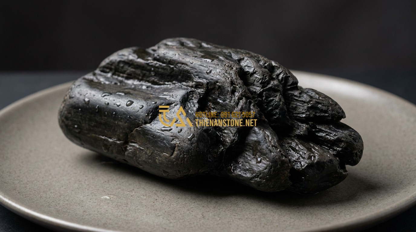 Tạo ảnh tiếng Anh: Close-up shot of a single, intricately shaped black driftwood stone. The surface shows smooth worn areas contrasted with sharp, deep natural grooves. Raindrops glisten on the dark surface, highlighting the rich black tones. Professional studio lighting on a neutral background.