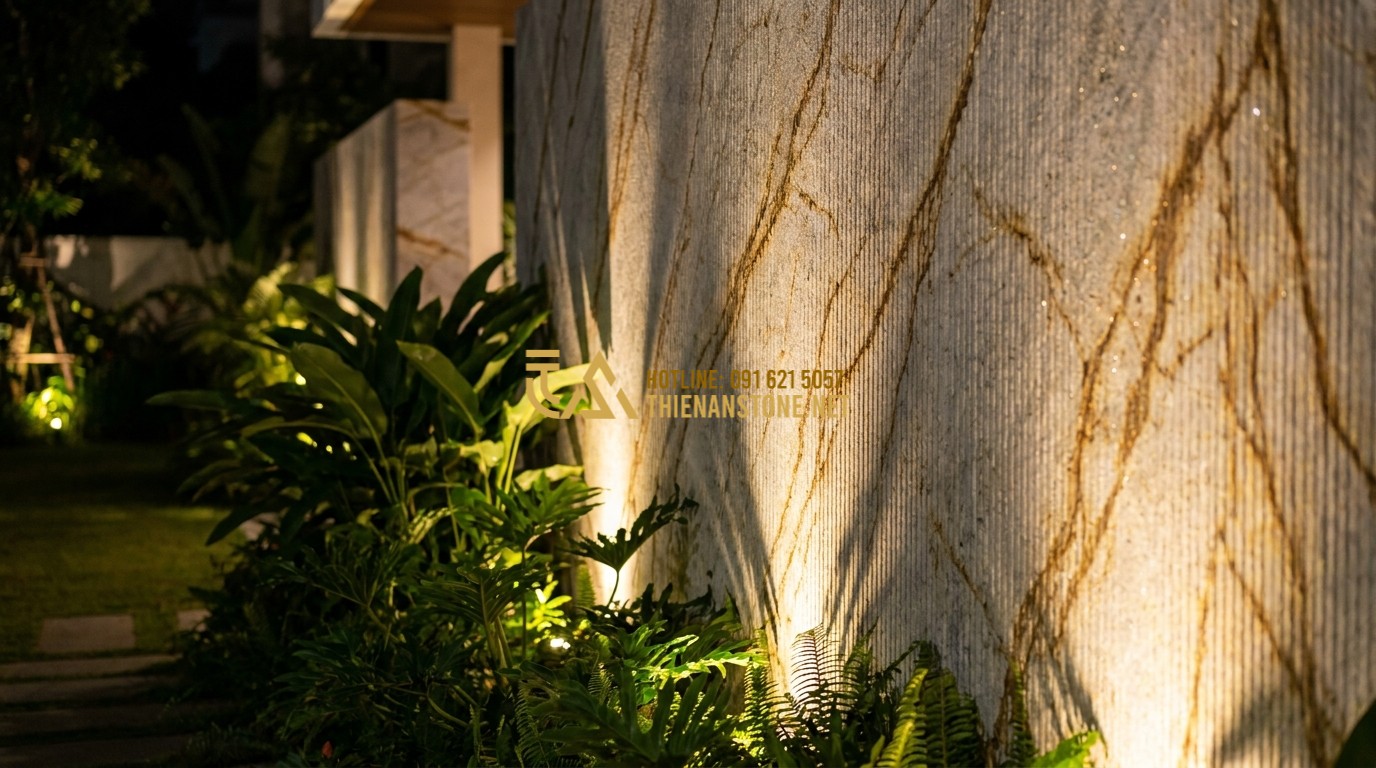 Tạo ảnh tiếng Anh: An outdoor wall of a luxury villa at night, decorated with yellow comb-textured stone. Golden LED spotlights cast shadows along the vertical grooves, highlighting the natural mineral glints of the stone. Lush green plants are nearby, creating a warm and elegant outdoor ambiance.