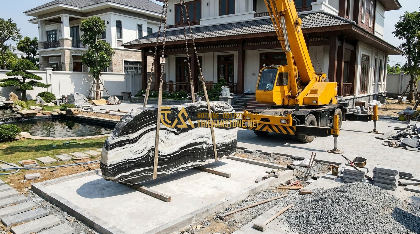 Tạo ảnh tiếng Anh: A professional team from Thien An Stone using a large crane to carefully position a massive Tuyet Son stone in a luxury villa's front yard. Workers are wearing safety gear and showing high expertise. Bright daylight, active construction scene.