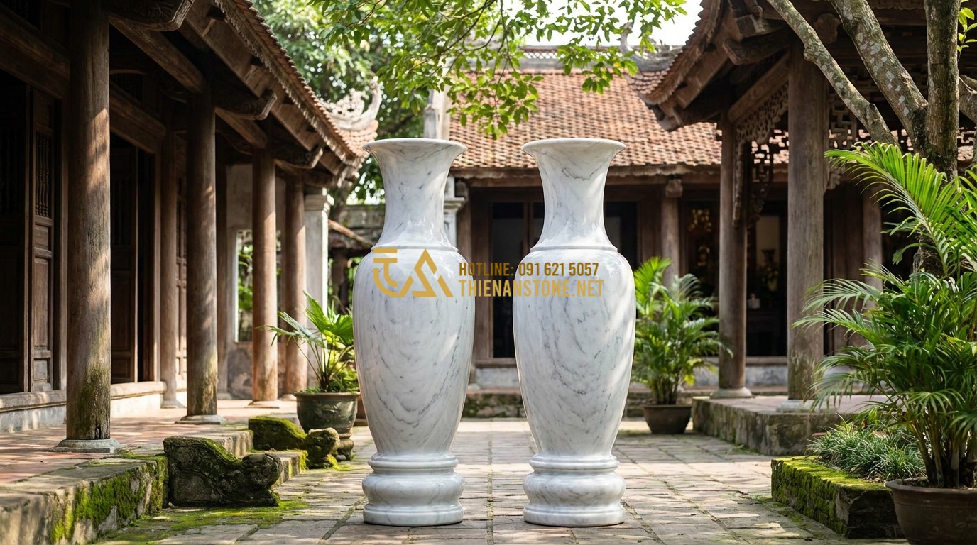 Tạo ảnh tiếng Anh: A pair of majestic, large-scale natural marble water hyacinth vases (Luc Binh Da) standing in a traditional Vietnamese courtyard with ancient wooden architecture. The stones feature intricate natural veins in shades of white and grey. Professional photography, cinematic lighting, 8k resolution.