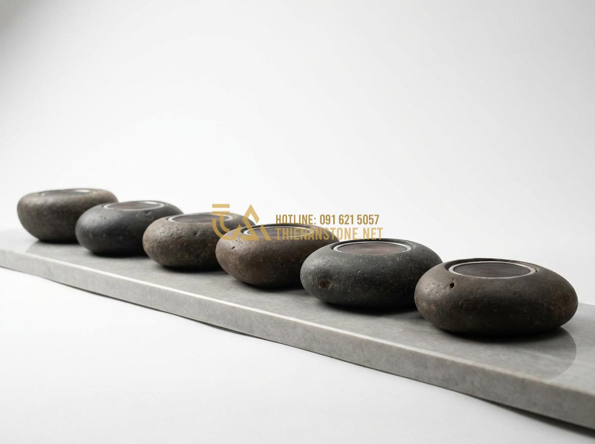 Tạo ảnh tiếng Anh: Beautiful variety of different mini infrared stone tea stoves displayed in a row on a stone showroom shelf, various natural stone colors and shapes, professional product catalog photography, clean white background, soft studio lighting highlighting textures and details, high-end luxury feel, 8k ultra detailed