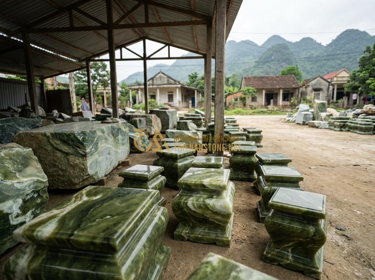 Create a professional wide-angle photograph of the exterior of Xưởng Đá Mỹ Nghệ Thiên An workshop in Phu Tho province, Vietnam, showing stone blocks and finished chân tảng đá pedestals displayed outdoors under natural daylight, traditional Vietnamese rural setting with mountains in background, documentary style, high detail 8k resolution