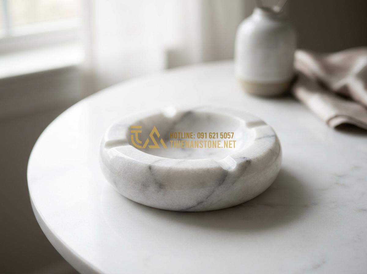Tạo ảnh tiếng Anh: Close-up professional studio shot of various natural stone ashtrays in different colors and shapes including round granite, square marble, and carved basalt designs, arranged elegantly on a white marble surface with soft natural light casting gentle shadows to highlight textures and veins, luxury product photography style, high detail, 8k resolution, clean minimalist composition