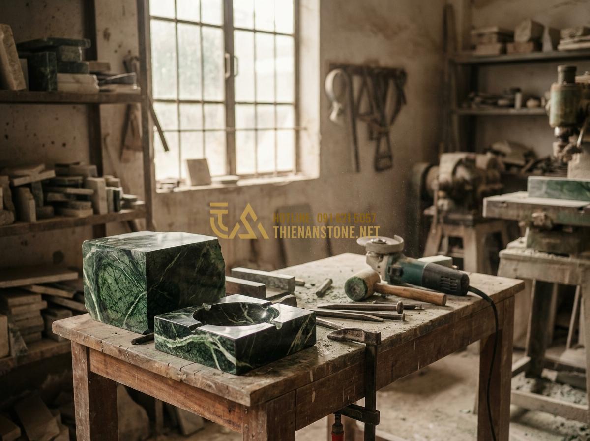 Tạo ảnh tiếng Anh: Detailed behind-the-scenes view inside a professional stone workshop in Vietnam, skilled artisans hand-carving a natural stone ashtray from a large granite block using traditional tools and modern machinery, dust particles in the air, focused lighting on the work in progress, realistic documentary photography style, high resolution, warm earthy tones