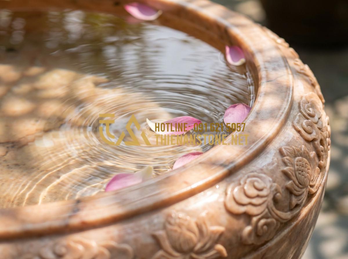 Lu nước phong thủy: Bí quyết đặt lu nước trước nhà để rước tài lộc, vượng khí - Hình 7 Lu nước phong thủy: Bí quyết đặt lu nước trước nhà để rước tài lộc, vượng khí - Tạo ảnh tiếng Anh: Close-up of water ripples inside a stone jar, with a few pink